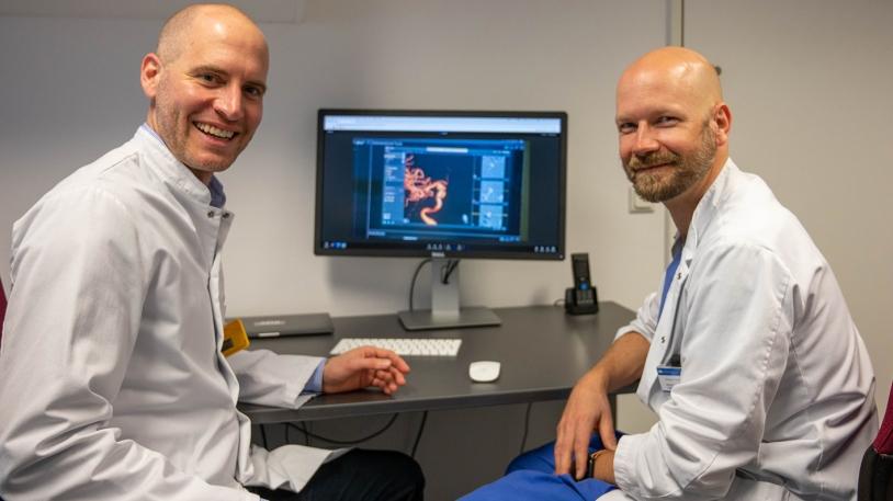 Dr. Benedikt Schwaiger links und Dr. Tobias Boeckh-Behrens rechts vor Schreibtisch sitzend; Blick in die Kamera 